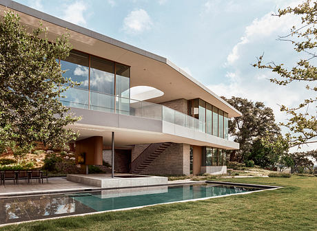 Modern glass and brick house with pool, surrounded by lush greenery.