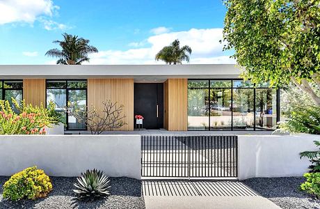 Modern home entrance with sleek wooden panels, glass walls, and lush tropical landscaping.