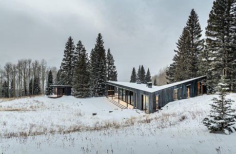 Sleek, modern structure with extensive glazing amidst snowy, pine-dotted landscape.