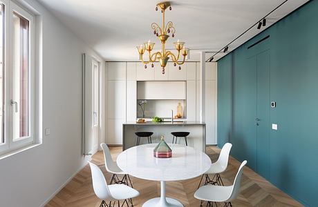 Modern open-plan kitchen and dining area with sleek cabinets, circular table, and elegant chandelier.