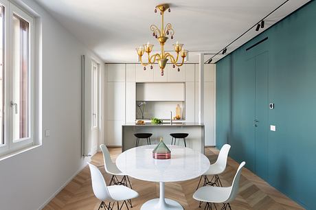 Modern open-plan kitchen and dining area with sleek cabinets, circular table, and elegant chandelier.