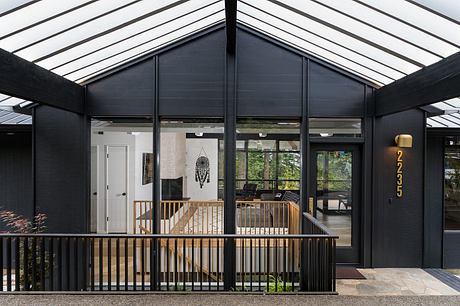 A modern, glass-enclosed house with a wooden deck, metal railings, and a black exterior.