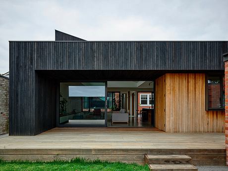 A modern architectural design featuring a dark wooden exterior, large windows, and a raised deck.