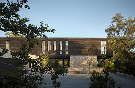 A modern, wood-paneled building with large windows and a covered entrance, surrounded by lush greenery.