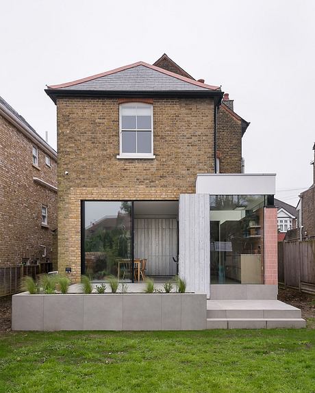 A modern brick home with a glass extension, raised concrete planters, and a minimalist aesthetic.