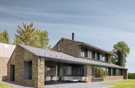 Modern stone-clad farmhouse with sleek lines, large windows, and covered outdoor living space.