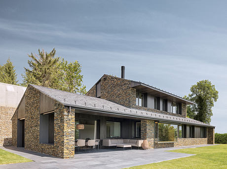 Modern stone-clad farmhouse with sleek lines, large windows, and covered outdoor living space.