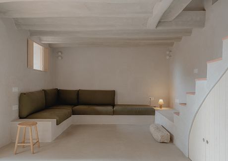 White interior with rustic wooden ceiling beams, L-shaped sofa, and simple furnishings.