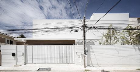 A modern, minimalistic residential building with a white façade, metal gate, and overhead cables.