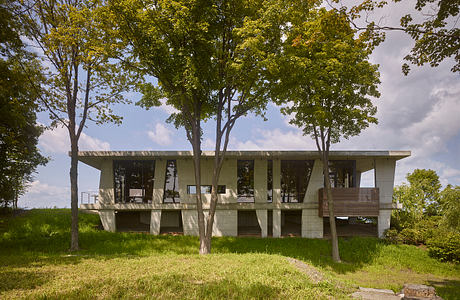 A modernist concrete structure with large windows, surrounded by lush greenery.