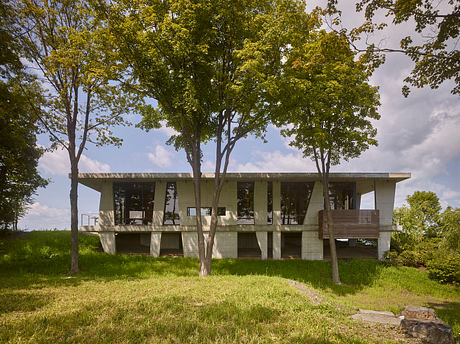 A modernist concrete structure with large windows, surrounded by lush greenery.