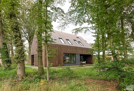 A modern wooden structure with large windows nestled among lush green trees.