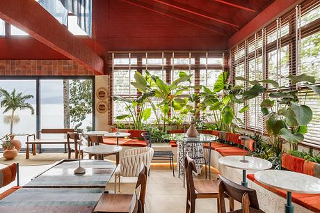 A warm, tropical-inspired cafe interior with vibrant red walls, lush greenery, and natural wood furnishings.