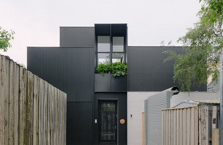 Modern, minimalist architecture with dark exterior, greenery, and stone walkway.