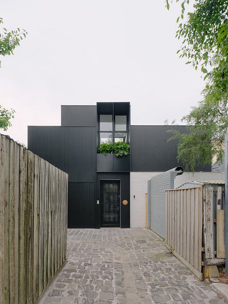 Modern, minimalist architecture with dark exterior, greenery, and stone walkway.