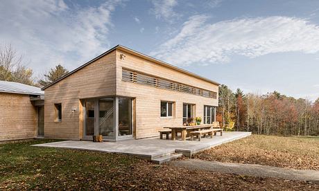 A modern, wooden-clad house with large windows and a spacious outdoor terrace.