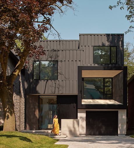 A modern, two-story home with a mix of dark panels, large windows, and wooden accents.