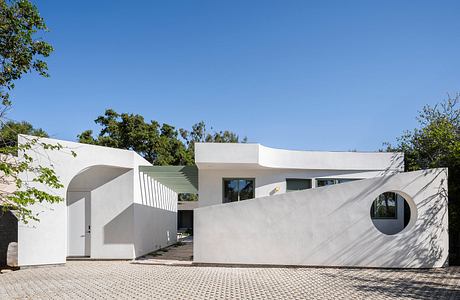 Modernist residential building with curved walls, large windows, and a paved courtyard.