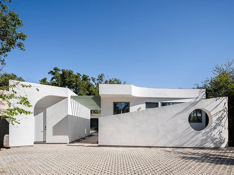 Modernist residential building with curved walls, large windows, and a paved courtyard.