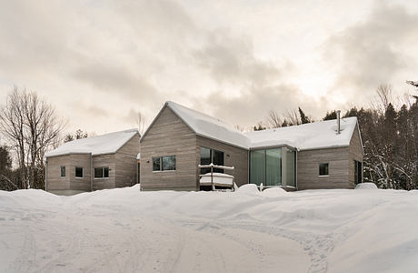 Sophisticated modern wooden cabin with expansive windows overlooking snowy landscape.