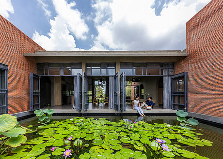 A modern brick building with a tranquil courtyard featuring a pond and lush lily pads.