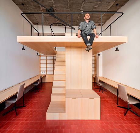 A modern, minimalist interior with a raised platform, wooden furniture, and a brick floor.