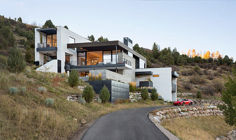 A modern, multilevel home nestled in a forested hillside, with sleek lines, balconies, and a red sports car.