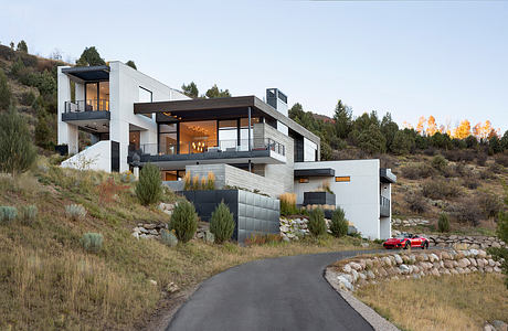 A modern, multilevel home nestled in a forested hillside, with sleek lines, balconies, and a red sports car.