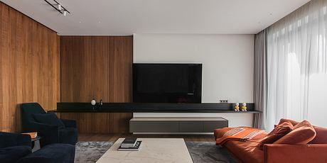 Sleek, modern living room with wooden paneling, minimalist TV console, and plush orange sofa.