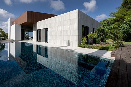 A modern concrete and wood residential building with a pool and surrounding landscape.