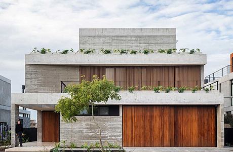 A modern, concrete building with a wooden facade, large windows, and lush landscaping.