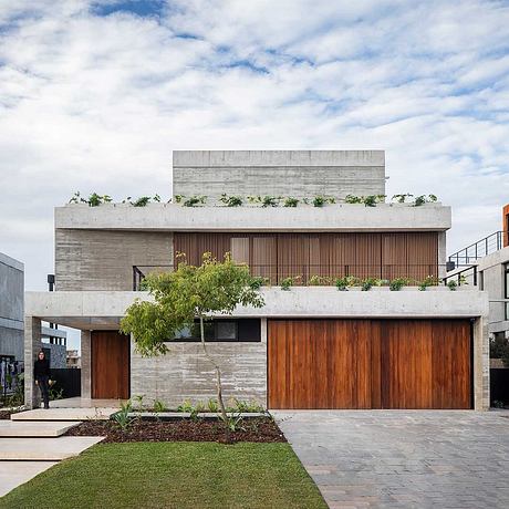 A modern, concrete building with a wooden facade, large windows, and lush landscaping.