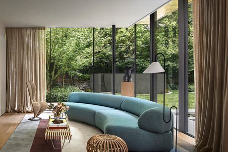 A modern, minimalist living room with large windows overlooking lush greenery outside.