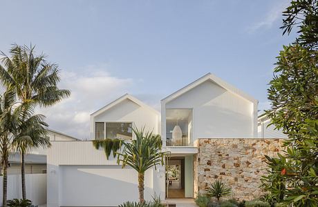 Modern tropical villa with sleek white facade, stone accent wall, and lush landscaping.