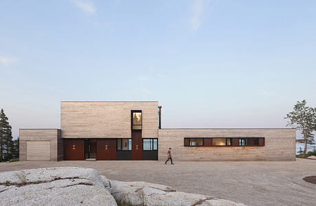 A modern, boxy structure with clean lines, wood panels, and large windows overlooking nature.