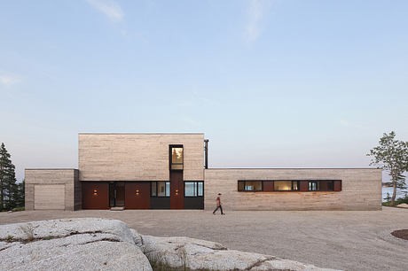 A modern, boxy structure with clean lines, wood panels, and large windows overlooking nature.