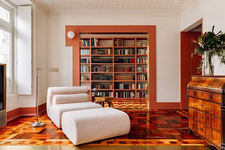 A cozy and inviting library nook with built-in bookcases, plush seating, and a patterned hardwood floor.