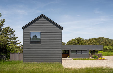 A modern, gray-clad house with clean lines, large windows, and surrounded by lush greenery.