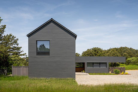 A modern, gray-clad house with clean lines, large windows, and surrounded by lush greenery.