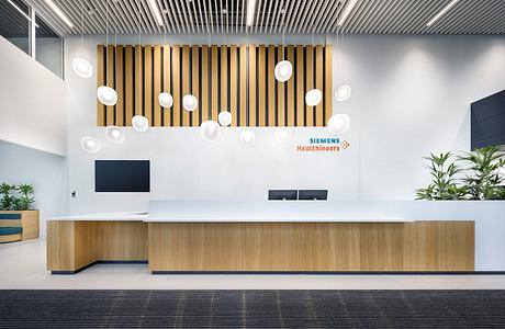 Modern office lobby with sleek wooden slat wall, circular pendant lights, and minimalist reception desk.