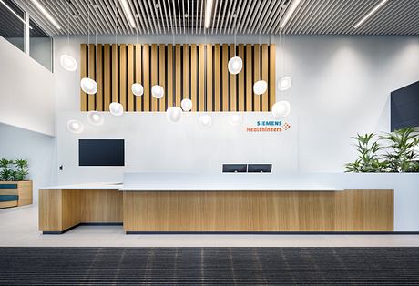 Modern office lobby with sleek wooden slat wall, circular pendant lights, and minimalist reception desk.