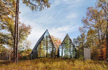 Two triangular glass structures amidst the autumn foliage, showcasing modern architectural design.