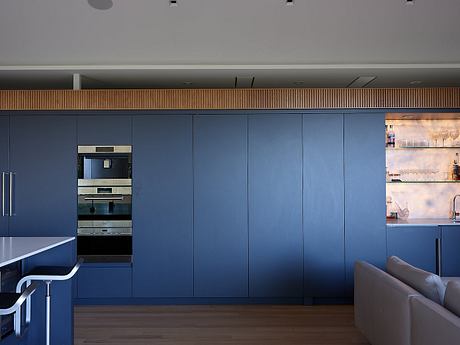 The image depicts a modern kitchen with sleek, dark blue cabinetry, stainless steel appliances, and a warm wood ceiling detail.