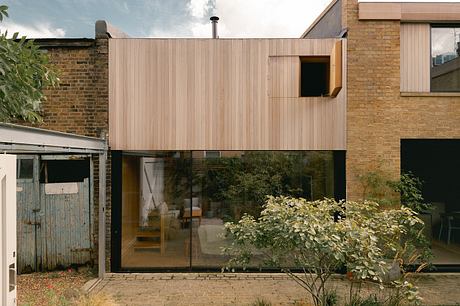 Modern wooden exterior with large glass windows overlooking a lush garden.