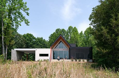 A modern, glass-fronted home with a wooden and concrete exterior, surrounded by lush greenery.