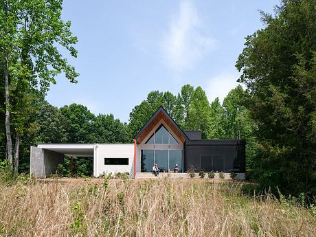 A modern, glass-fronted home with a wooden and concrete exterior, surrounded by lush greenery.