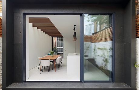 A modern, minimalist interior with a wooden staircase, dining table, and large windows.