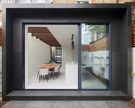 A modern, minimalist interior with a wooden staircase, dining table, and large windows.