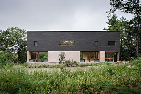 A modern, minimalist two-story home with large windows and a natural landscape backdrop.