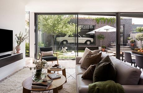 Sleek modern living room with floor-to-ceiling glass doors, lush outdoor garden, and vintage car.